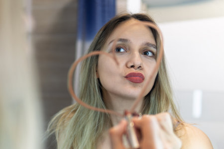 The concept of loving yourself, self-love. A young beautiful woman draws a heart with lipstick on the mirror in the bathroom at home.の写真素材