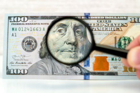 Counterfeiter forges banknotes. Fake concept. Fake money American dollars, magnifier. view money under a magnifying glass. watermark, water mark. search for counterfeit billsの写真素材