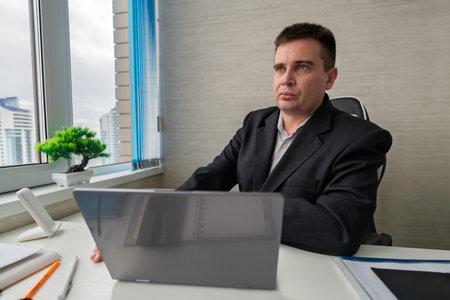 Professional Man Working on a Laptop at a Modern Office Desk During the Daytime in a Stylish...