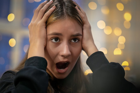 screaming teenage girl holding her head With his mouth wide open on a dark blurred background with...