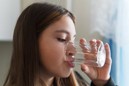 A teenager girl drinks water from a glass in the kitchen