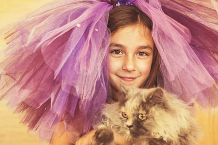 Girl dressed in purple with a funny hat holding a cat in her handsの写真素材
