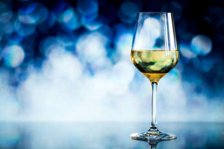 glass of white wine against a glowing bokeh - copy space, selective focusの写真素材