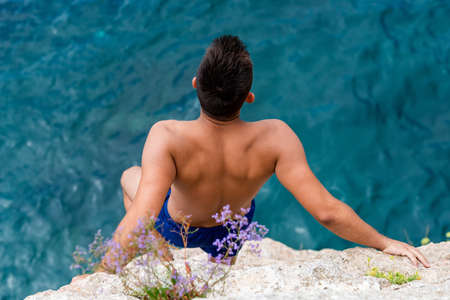 Young man gaining courage before  jumping in to the sea from high rocksの写真素材