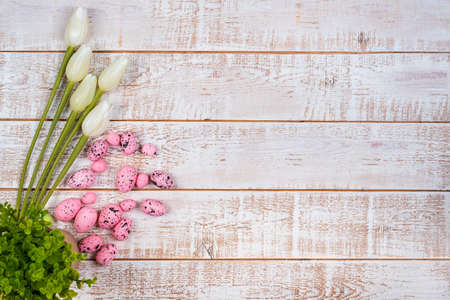 Easter background with colorful eggs and tulips over white wooden table - copy space
