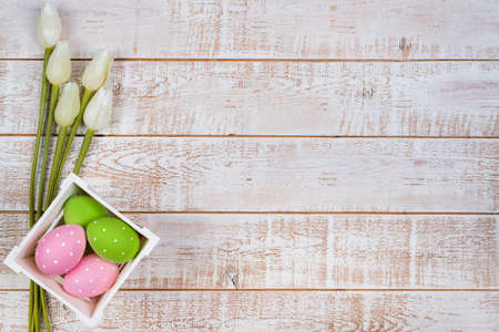 Easter background with colorful eggs and tulips over white wooden table - copy spaceの写真素材