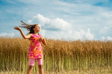 Happy little girl in a field of ripe rapeseed - selective focus, copy spaceの写真素材