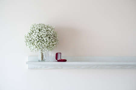 Wedding rings in a red velvet box and bridal bouquet over a white shelf - selective focus, copy spaceの写真素材
