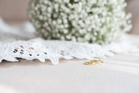 Wedding rings and a bridal bouquet over a white lace wedding dress - selective focus, copy spaceの写真素材