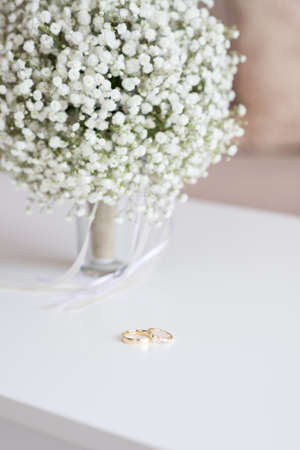 Wedding rings and bridal bouquet over a white table - selective focus, copy space, vertical...