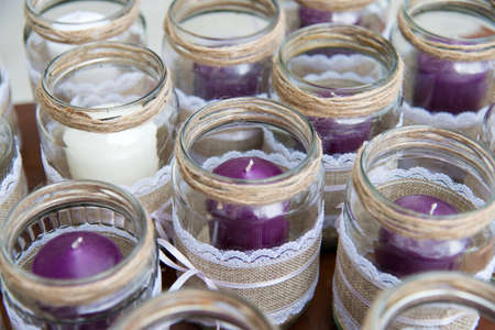 Wedding decoration - candles in glass jars decorated with lace, sackcloth and ribbons over wooden...