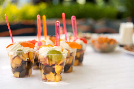 Catering for party. Close up of appetizers with peaches, plums, grapes and cream in short glasses on white table.の写真素材