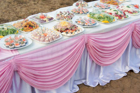 Buffet catering for a wedding party on the beach on a white table with a pink draperyの写真素材
