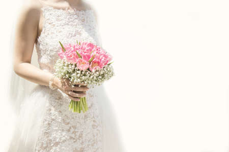 Beautiful bride in a wedding dress holding a bouquet of pink tulips. White background. Text space.の写真素材
