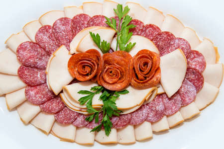 Different types delicacies of meat and cheese arranged in a plate over light background - selective...