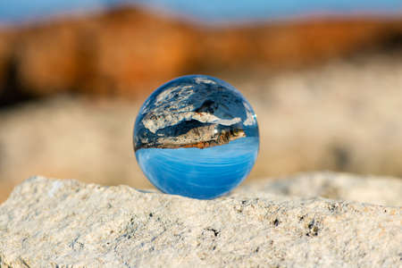 Upside down seascape with blue sky and overgrown with moss rocks - reflection in a lensball - selective focus, space for textの写真素材