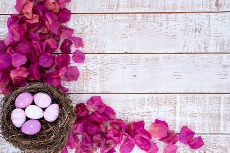 Easter background with colorful eggs in a nest over white wooden rustic table - copy space
