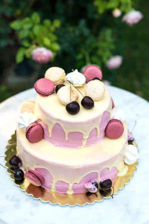 Fruit cake decorated with cherries and French macaroni served on a marble table against the...