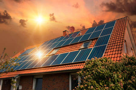 Photo collage of solar panels, photovoltaics on the red roof of a house and a beautiful sky with the...