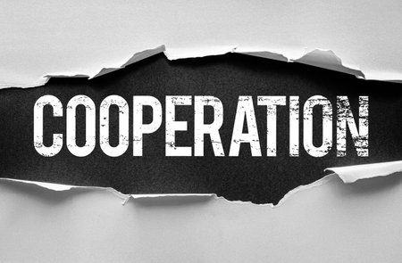 The word "COOPERATION" in bold, distressed white letters is revealed beneath torn paper on a black background. Conceptual image symbolizing teamwork, unity, partnership, and collaborationの写真素材