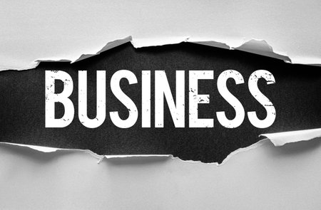 Word BUSINESS in bold textured letters appears beneath torn paper strips. Creative concept representing commerce, finance, entrepreneurship, or company-related themes with dramatic layoutの写真素材