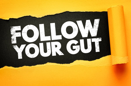 Inspirational phrase "FOLLOW YOUR GUT" in bold white distressed letters on a black background, revealed through torn yellow paper, symbolizing intuition, decision-making, and inner confidenceの写真素材