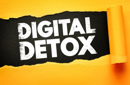 Grunge white text "DIGITAL DETOX" on a black background revealed through torn yellow paper. Symbolizes unplugging, mindfulness, and tech-free lifestyle. Clean and powerful visual conceptの写真素材