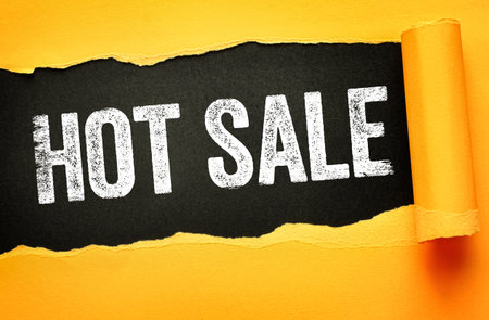 HOT SALE text revealed through ripped yellow paper against a black background. Eye-catching promotional graphic for discounts, clearance, flash deals, marketing, or retail eventsの写真素材