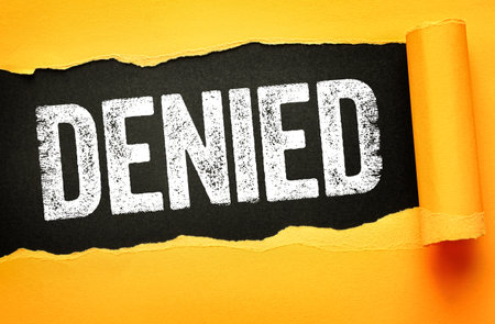 DENIED in bold, distressed white text on a dark black background revealed through torn yellow paper. Concept of rejection, refusal, blocked access, disapproval, failure, or declineの写真素材