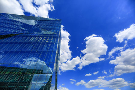 Modern glass building with striking reflections under vibrant blue sky with fluffy clouds....