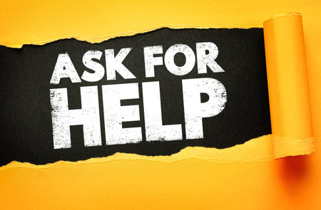 Bold white text ASK FOR HELP revealed through torn yellow paper on black background. Concept for support, guidance, assistance, outreach, advice, teamwork, or seeking help in tough situationsの写真素材
