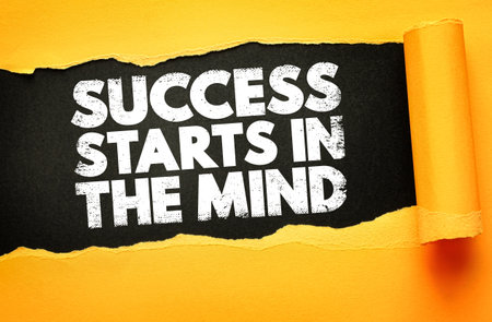 Motivational phrase SUCCESS STARTS IN THE MIND revealed under torn yellow paper on black background. Bold distressed text emphasizes mental strength and mindset for personal growthの写真素材