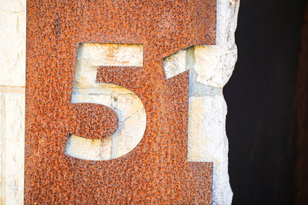 Rusty metal number 51 cut out from a weathered steel plate, revealing a light stone wall beneath. The rugged texture and contrast between the rusted metal and stone surface evoke an industrial aestheticの写真素材