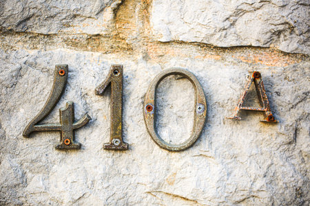 Rusty metallic house number 410A mounted on a textured stone wall. Aged patina and weathered screws add vintage charm and architectural character, perfect for rustic address or urban decay conceptsの写真素材