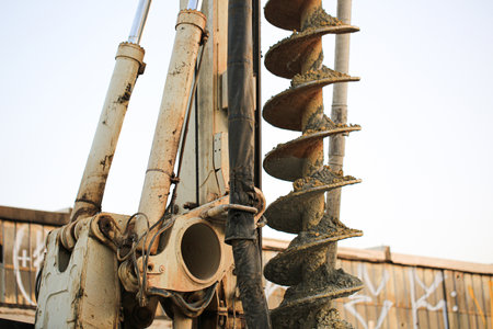 Close-up of an industrial drilling machine with auger bit coated in soil, used for ground excavation...