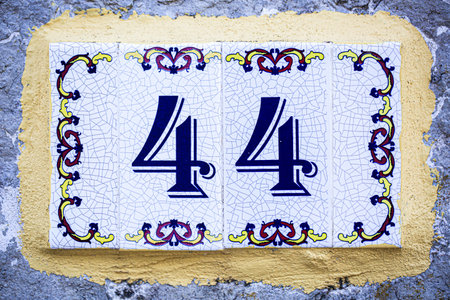 Ceramic tile house number 44 in a classic decorative style. The ornate floral border and cracked...