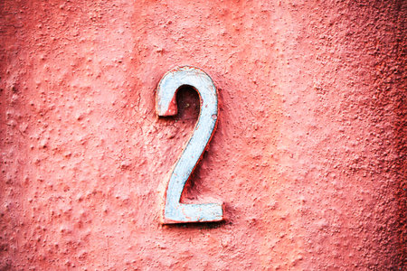 Weathered blue number 2 affixed to a textured coral-colored wall. The worn paint and bold contrast make it ideal for concepts involving signage, urban detail, numbers, or typographyの写真素材