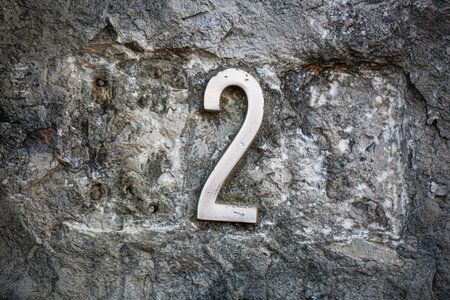 White metallic number 2 affixed to a rugged, textured stone surface. The contrast between the sleek,...