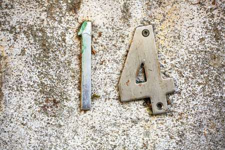 Metallic house number 14 affixed to a weathered, speckled white wall. The number shows signs of wear...