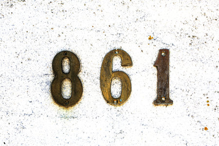 Rustic house number 861 in bold numerals on textured white stucco wall. Classic, minimal style with...