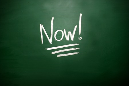 The word Now! on blackboard. A time management conceptの写真素材