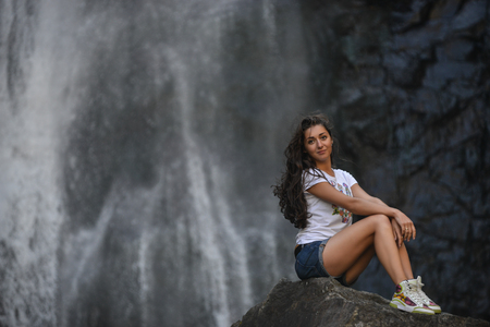 beautiful girl on rock with waterfall backgroundの写真素材