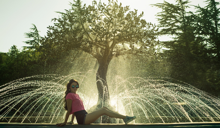 Beautiful brunette woman in glasses sitting on the fountainの写真素材