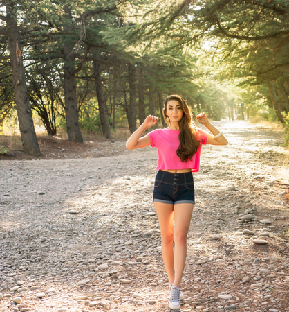Beautiful young woman in shorts against the sun background standing on stone pathの写真素材
