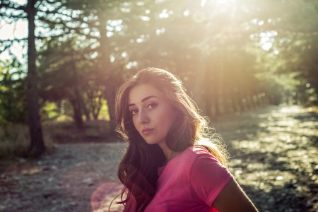 portrait of beautiful young woman in shorts against the sun background standing on stone pathの写真素材