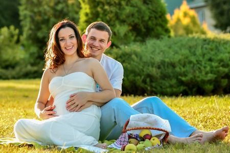 Happy pregnant couple sitting on the grass in the parkの写真素材