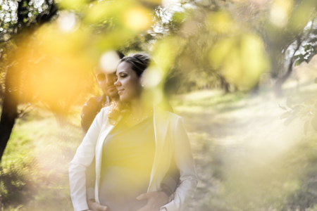 young pregnant couple sitting on yellow leaves in the park in autumnの写真素材