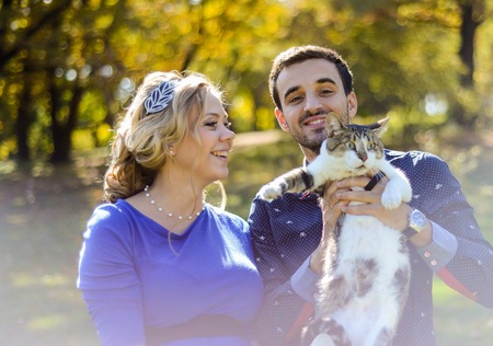 Happy and young pregnant couple hugging in nature and holding the catの写真素材