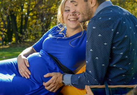 Happy parents expecting baby, pregnant woman with husband touching belly, sitting on green grass, body part, young family and new life conceptの写真素材