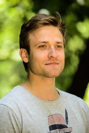 a young man in  T-shirt posing in park near tree